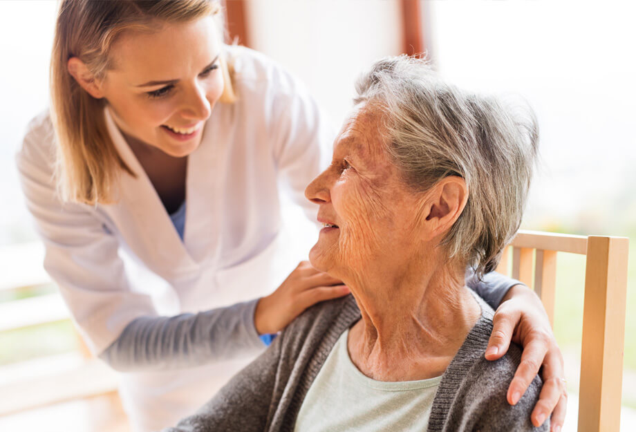 Caregiver smiling at older woman in a bright living space.