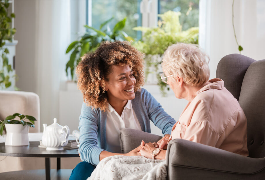 Caregiver smiling and holding hands with a senior woman in a comfortable living area.