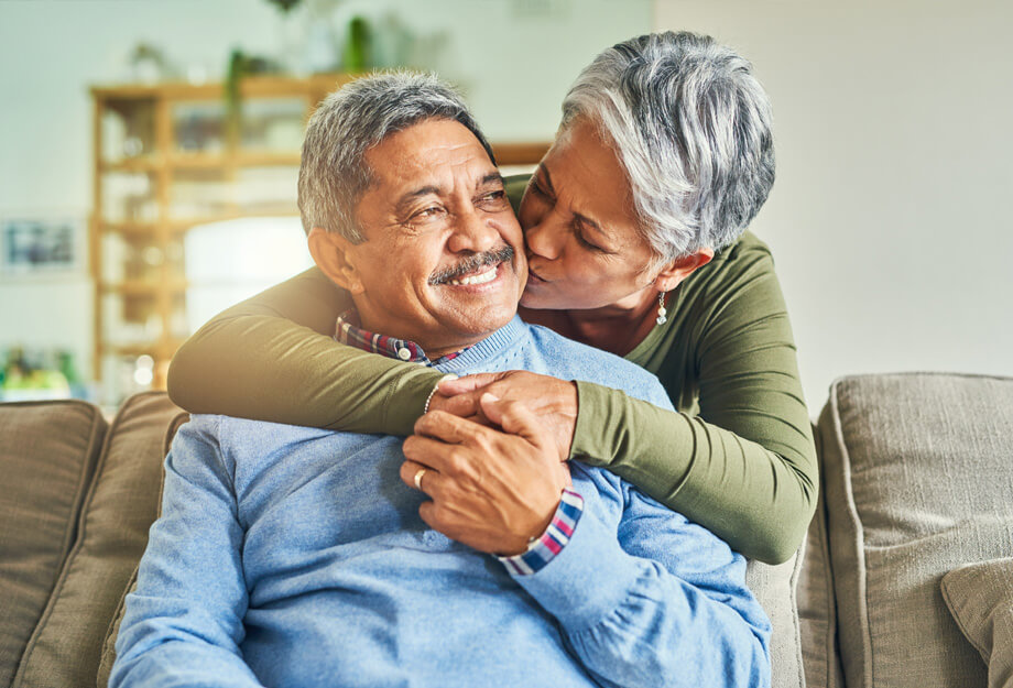 Elderly couple embracing in a cozy living room environment with warm lighting.