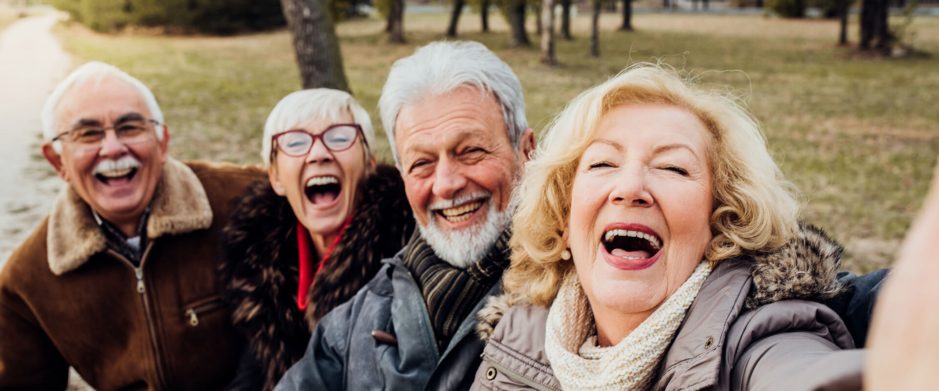 Four smiling seniors walking together outdoors on a sunny day.