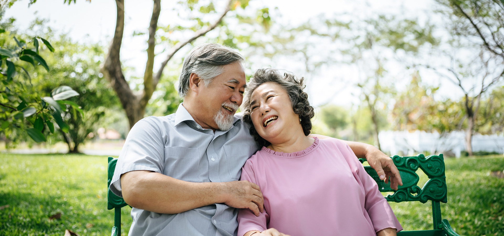 Elderly couple laughing together on a park bench on a sunny day.