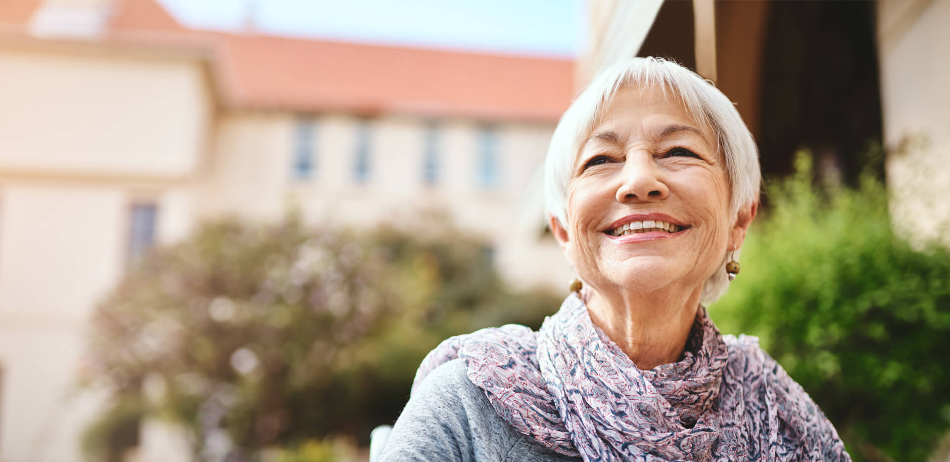 Smiling elderly woman outside with blurred building in the background.